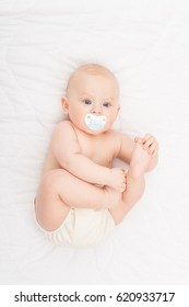 Cute blond baby boy in diaper with pacifier. High angle view of cute baby lying in bed. Studio lighting, medium retouch.