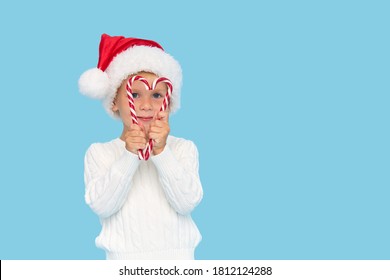 A cute blond baby boy in a Santa Claus hat holding a heart-shaped lollipop cane on a blue background. Heart health concept in children - Powered by Shutterstock