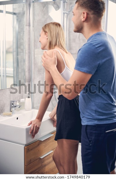 Cute blond female looking in mirror near sink while brunette Caucasian male...