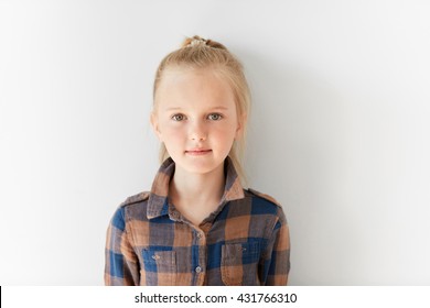 Cute blond girl posing on white background. Portrait of relaxed kid with nice kind look. Calm and pretty little Caucasian girl with pony-tail in brown shirt. Childish innocence, free and happy life.