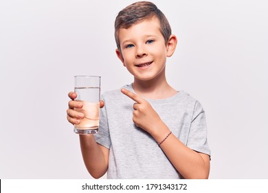 Cute Blond Kid Drinking Glass Of Water Smiling Happy Pointing With Hand And Finger 