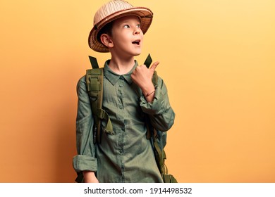 Cute Blond Kid Wearing Explorer Hat And Backpack Pointing Thumb Up To The Side Smiling Happy With Open Mouth 