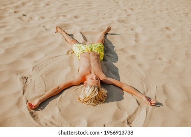 Junge Junge mit süßer Blondine in gelben Hosen, die auf dem Sandstrand liegen und den Engel spielen. Sommerzeitkonzept. Kopiert Platz.