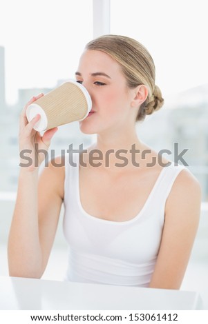 Cute blond woman in bright room drinking coffee