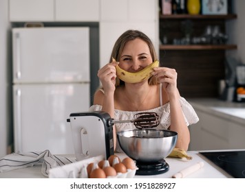 Cute Blond Woman In White Clothes Stay On Kitchen Hold Banana As A Smile. Chocolate Dough For Cake.  