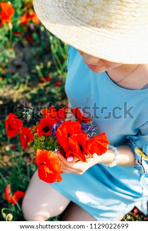 Cute blond young woman with braided hair in the field of red poppies and blue flowers