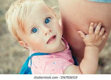 Cute Blonde Caucasian Girl Toddler With Blue Eyes Holding Mom And Looking At Camera. Closeup Of Curious Surprised Baby Face. Shy Toddler Child Scared Of Stranger. Cute Girl Kid With Parent Outdoor.