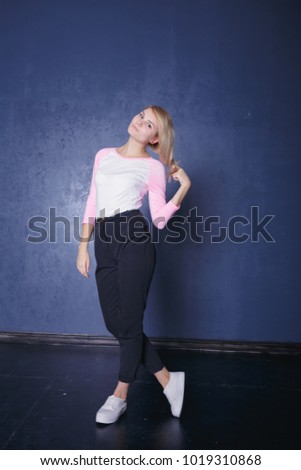 cute blonde girl having fun and fooling around on dark textured background. emotional portrait of a student. clean skin and long hair. street style in clothes: loose trousers and a colored jacket
