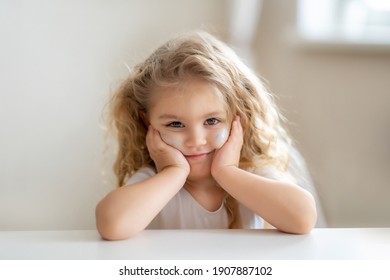  Cute Blonde Toddler Girl Sitting At The Table With Hand On Chin. High Quality Photo