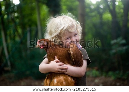 Cute blonde toddler hugging a brown hen