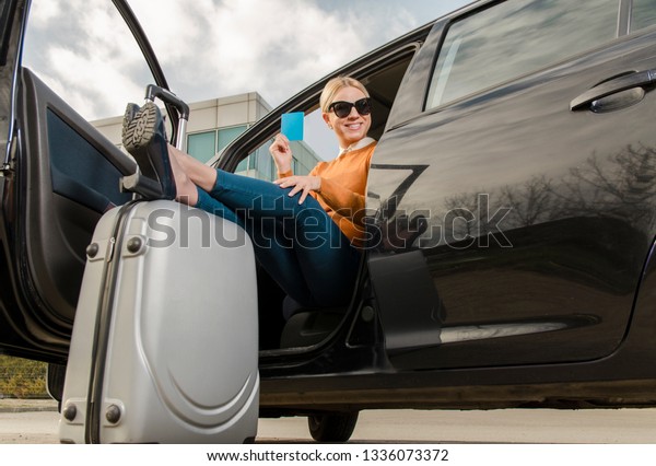 Cute blonde with travel\
insurance / passport , legs on suitcase sitting in a car. Happy\
traveler 