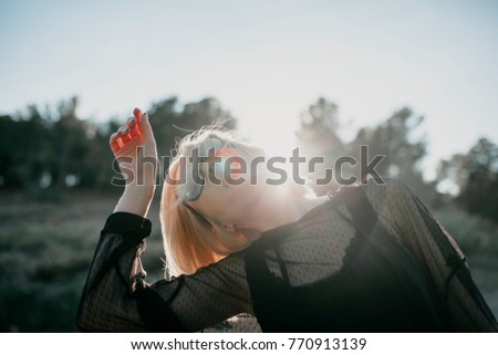 Blonde woman with black dress and sunglasses performing dance in nature with backlight