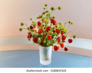 Cute bouquet of ripe wild strawberries stands on a glass table. Close-up. Branches of wild strawberries have just been plucked from a clearing in forest. Natural still life with red and green berries.