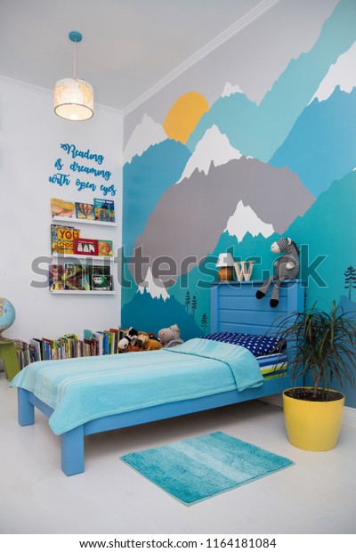 Cute boy bedroom wallpaper design with a turquoise grey mountain wall mural and lots of books.