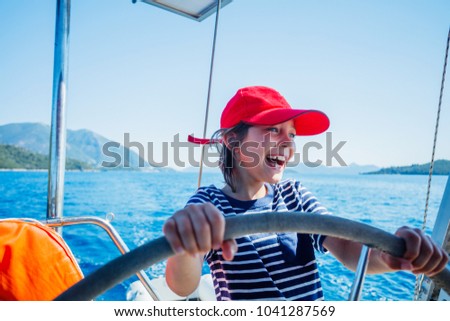 Cute boy captain on board of sailing yacht on summer cruise. Travel adventure, yachting with child on family vacation. Kid clothing in sailor style, nautical fashion.