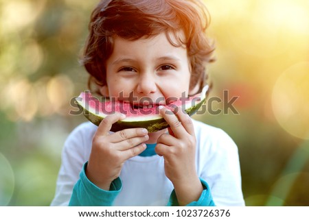Cute boy child eating healthy organic watermelon in garden, nature background, sunny lights