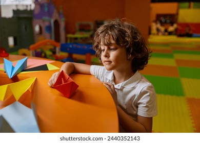 Cute boy child playing handmade origami paper boat at childcare center - Powered by Shutterstock