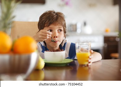 Cute boy drinking orange juice and eating muesli for breakfast