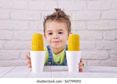 Cute Boy Eating Boiled Sweet Corn On White Bricks Wall Background.