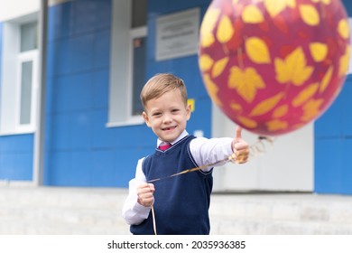 Cute Boy First Grader At School With A Balloon In His Hand On A Sunny Autumn Day. Celebration On September 1st. Knowledge Day. Selective Focus