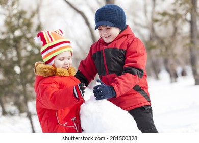 Cute Boy And Girl Building Snowman In Winter Park