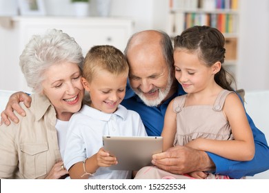 Cute boy and girl sitting in the lap of their grandmother and grandfather looking all at a PC tablet - Powered by Shutterstock