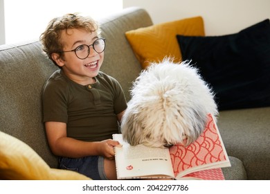 Cute boy with glasses, age 5, reads a story to his dog on the couch