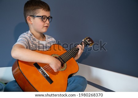 Cute boy with glasses learns to play the classical guitar at home.