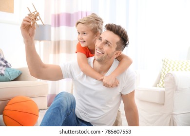 Cute Boy And His Father Playing With Toy Airplane At Home