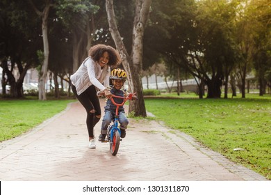 Cute Boy Learning To Ride A Bicycle With His Mother. Woman Teaching Son To Ride Bicycle At Park.