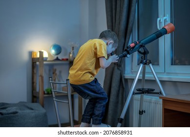 Cute boy is looking through a telescope in a room at the night starry sky. Children's scientific hobbies and space exploration