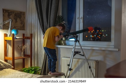 Cute Boy Is Looking Through A Telescope In A Room At The Night Starry Sky. Children's Passion For Space Exploration