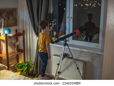 Cute Boy Is Looking Through A Telescope In A Room At The Night Starry Sky. Children's Passion For Space Exploration