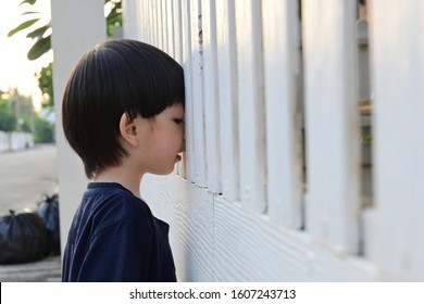 cute boy looking through white wooden front gate of home