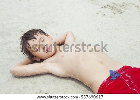 Cute boy lying on the beach and sunbathing. Child resting on a beach on a sunny day.