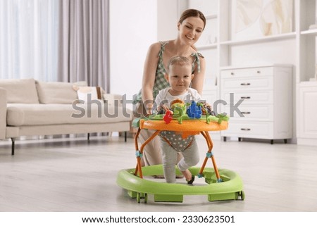 Cute boy making first steps with baby walker. Happy mother and her little son spending time together at home