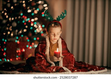 A cute boy is making a wish while holding a candle on christmas eve at home.
