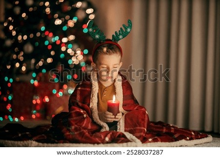 A cute boy is making a wish while holding a candle on christmas eve at home.