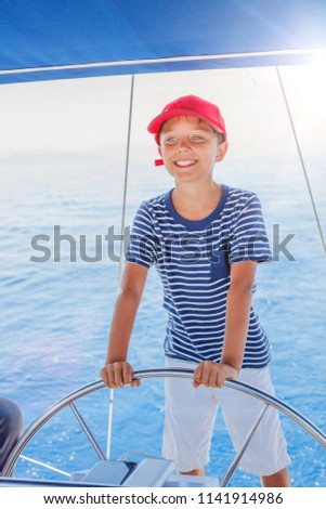 Cute boy on board of sailing yacht on summer cruise. Travel adventure, yachting with child on family vacation. Kid clothing in sailor style, nautical fashion.