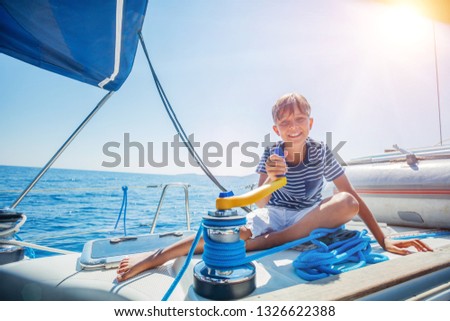 Cute boy on board of sailing yacht on summer cruise. Travel adventure, yachting with child on family vacation. Kid clothing in sailor style, nautical fashion. Focus on the Sailboat winch