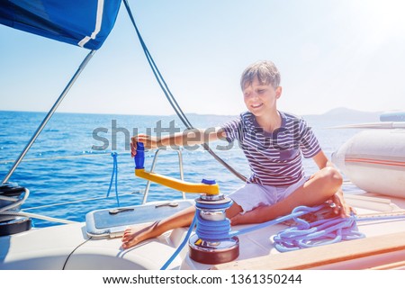 Cute boy on board of sailing yacht on summer cruise. Travel adventure, yachting with child on family vacation. Kid clothing in sailor style, nautical fashion. Focus on the Sailboat winch