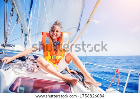 Cute boy on board of sailing yacht on summer cruise. Travel adventure, yachting with child on family vacation. Kid clothing in live vest.