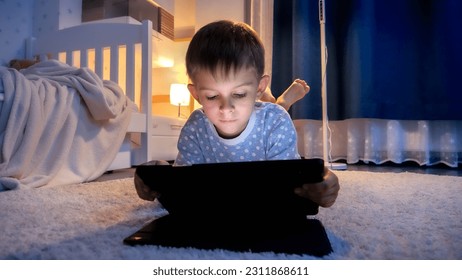 Cute boy in pajamas lying on floor in his room and using tablet computer before going to bed. Children education, development, kids using gadgets secrecy, privacy. - Powered by Shutterstock
