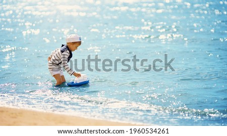 Cute boy playing with ship toy in the water at the sea.