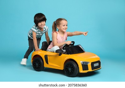 Niño lindo empujando el auto de juguete eléctrico de los niños con niña en fondo azul claro