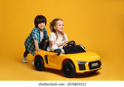 Niño lindo empujando el auto de juguete eléctrico de los niños con una niña de fondo amarillo