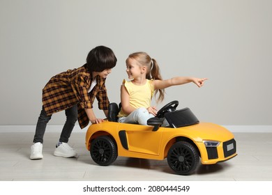 Cute boy pushing children's electric toy car with little girl near grey wall indoors - Powered by Shutterstock