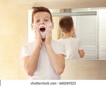 Cute Boy With Shaving Foam On Face Near Mirror In Bathroom