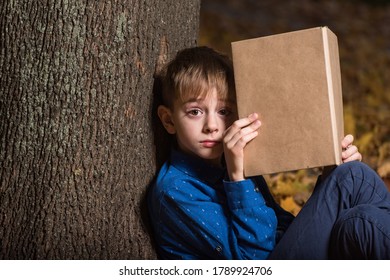 Cute Boy Sitting Near Tree With Book In Hands. Exciting Childrens Book. Copy Space. Mock Up