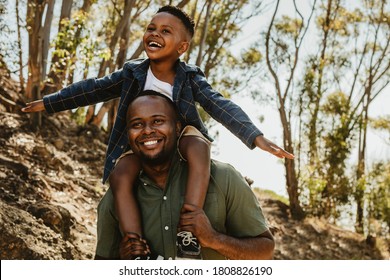 Cute boy sitting on his father's shoulder on a forest trail. Father and son enjoying on their holidays.